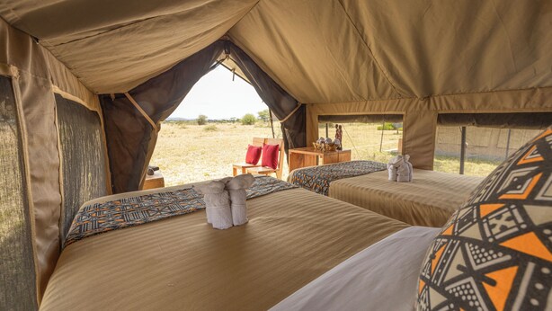 A tented accommodation with two beds, each with patterned pillows and a small table with a red chair.