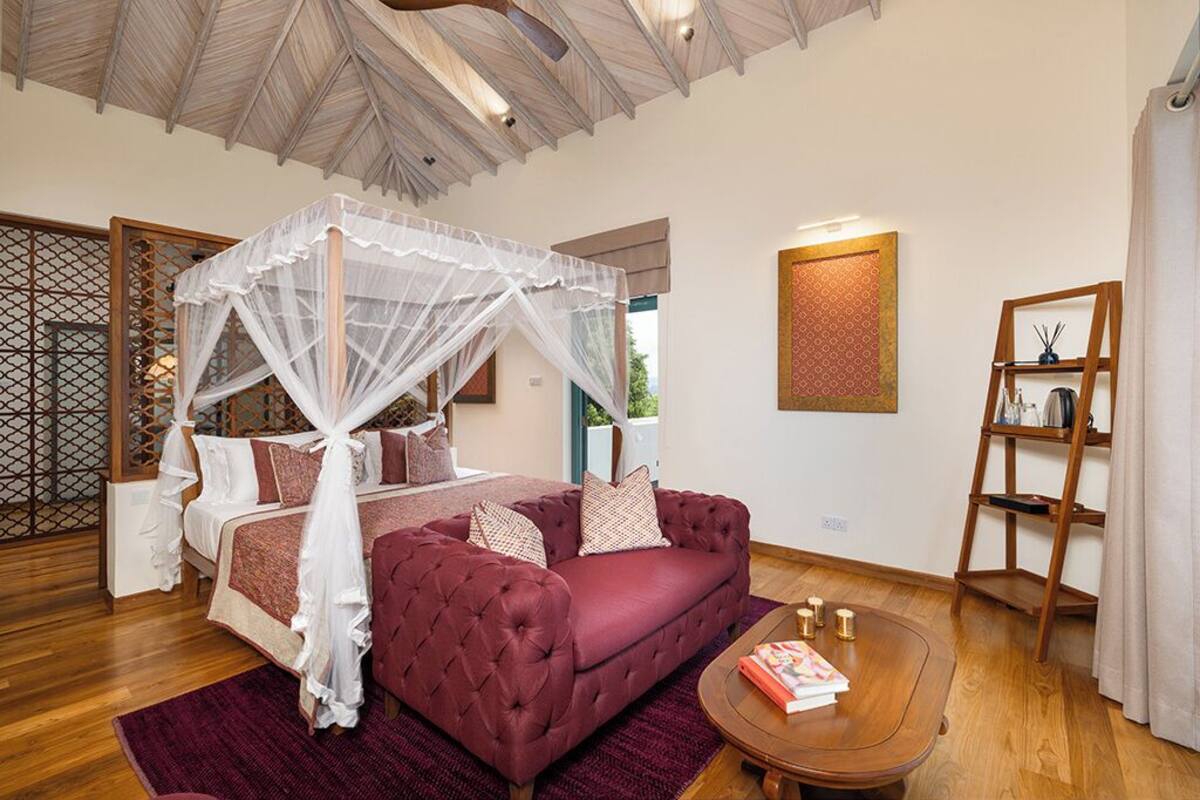 A bedroom with a four-poster bed, a red sofa, a wooden coffee table, and a decorative shelf.
