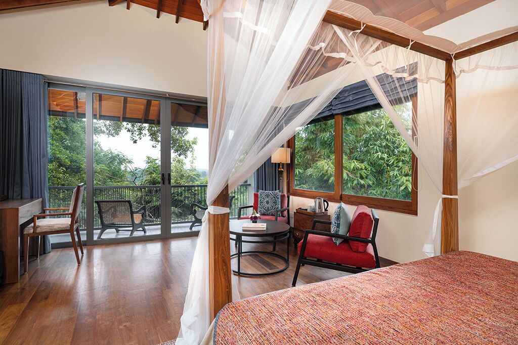 Un dormitorio con una cama grande, un balcón con una silla y vistas al verdor.