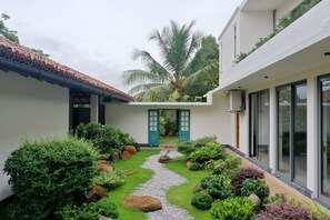 A modern building with a white exterior, a tiled roof, and a lush garden with a gravel path. - Heavensa Villas and Suites by The Clarks (Galle)