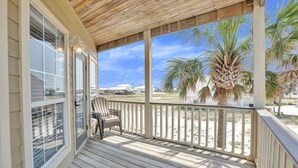 A wooden deck with a chair, overlooking a beach with palm trees and houses in the background. - Camp David 4 4 Pool Beach Views Sleeps 16 (Gulf Shores)