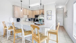 A modern kitchen with light wooden cabinets, a central island with bar stools, pendant lighting, and a refrigerator. - Camp David 4 4 Pool Beach Views Sleeps 16 (Gulf Shores)
