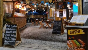 A wooden outdoor seating area with tables and chairs, a sign for 'Decanto do Porto', and a menu board advertising sushi. - Recanto do Porto Hotel (Porto Seguro)