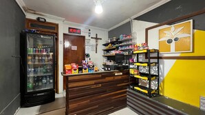 A small convenience store with a refrigerator stocked with beverages, shelves with snacks and other items, and a wooden counter. - Recanto do Porto Hotel (Porto Seguro)