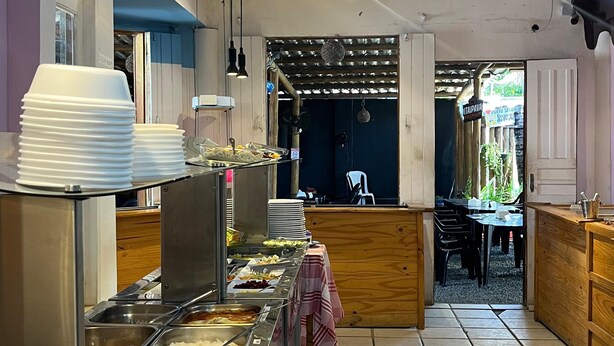 A buffet setup with various food stations, a ceiling fan, and a view into the dining area. - Recanto do Porto Hotel (Porto Seguro)