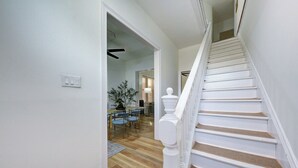 Una escalera con balaustres blancos y barandal de madera que conduce a un comedor con sillas azules y una mesa.