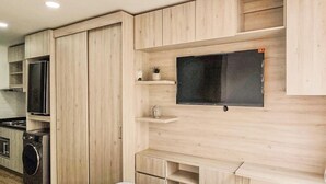 A modern hotel room with a bed, a TV mounted on the wall, a small kitchen area with a microwave and a washing machine, and wooden cabinetry. - Beautiful 5 star Loft - near Iserra 100 Bogota (Bogotá)