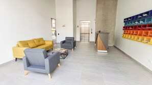 A modern reception area with a yellow sofa, grey armchairs, a small coffee table, and a reception desk with a wooden slat design. - Beautiful 5 star Loft - near Iserra 100 Bogota (Bogotá)
