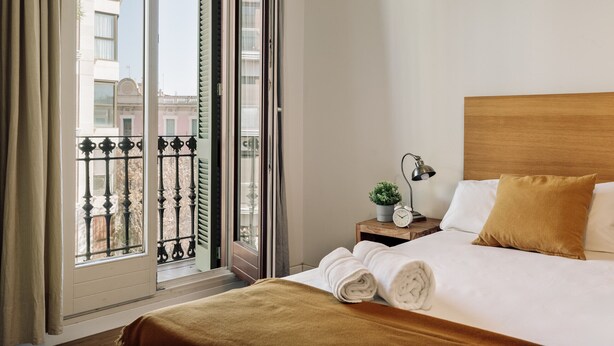 Ein Hotelzimmer mit Bett, Nachttisch, Lampe und Blick auf die Stadt durch ein Fenster.