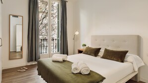 Ein ordentlich gemachtes Bett mit einer grünen Tagesdecke, ein Nachttisch mit Lampe und ein Fenster mit Vorhängen.