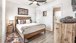 Une chambre avec un lit en bois, un ventilateur de plafond et une armoire en bois contenant des serviettes.