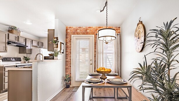 Une cuisine moderne avec un mur d’accent en briques, un coin repas avec une table et des chaises en bois, et un luminaire suspendu.