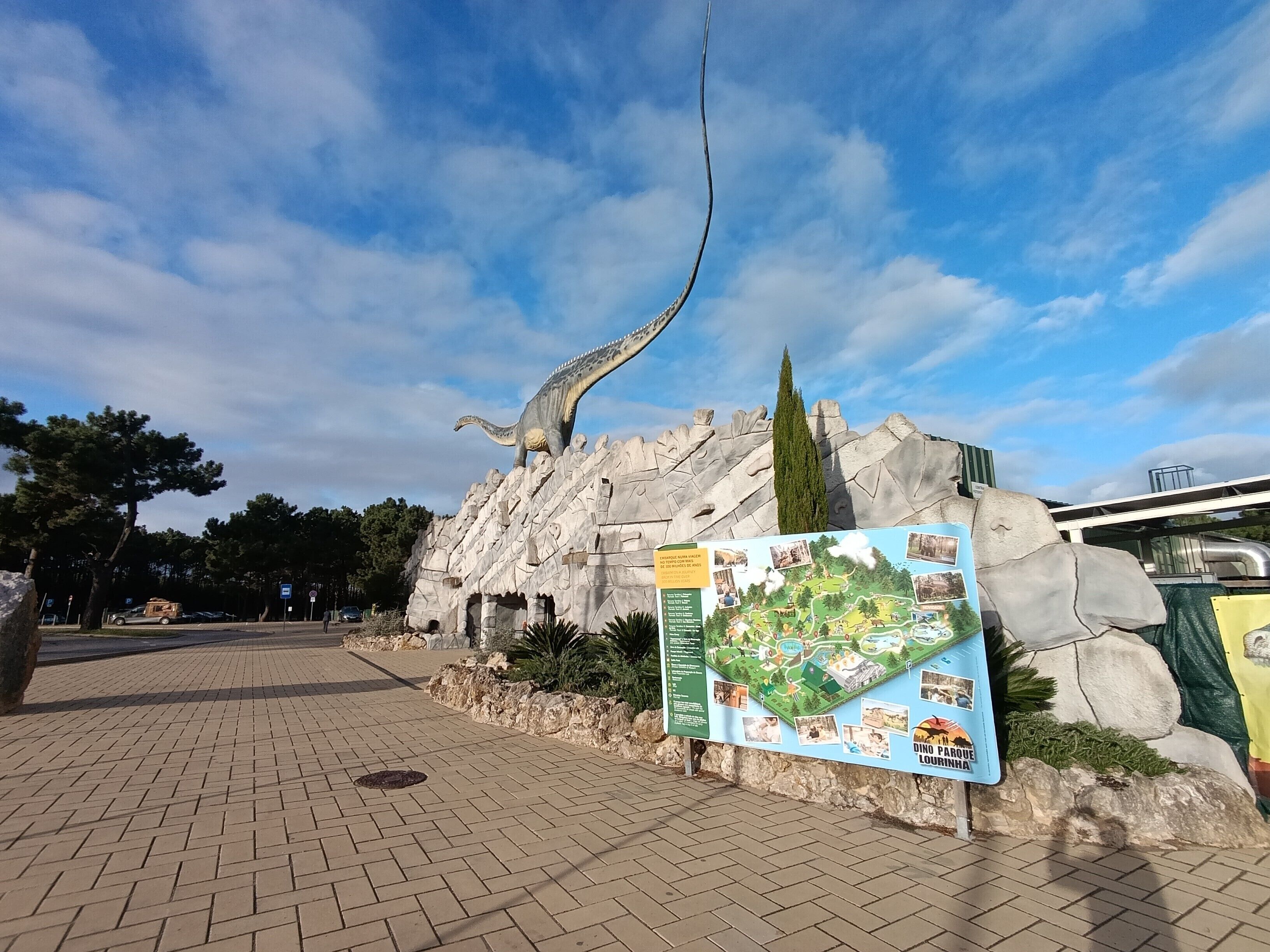 Eine Dinosaurier-Statue auf einer felsigen Klippe, im Vordergrund ein Wegweiser mit einer Karte.