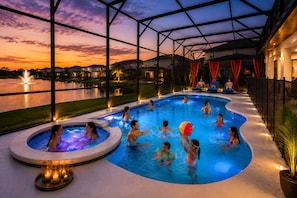 Una piscina con vista su un tramonto su un corpo d'acqua, circondata da un'area coperta con posti a sedere.