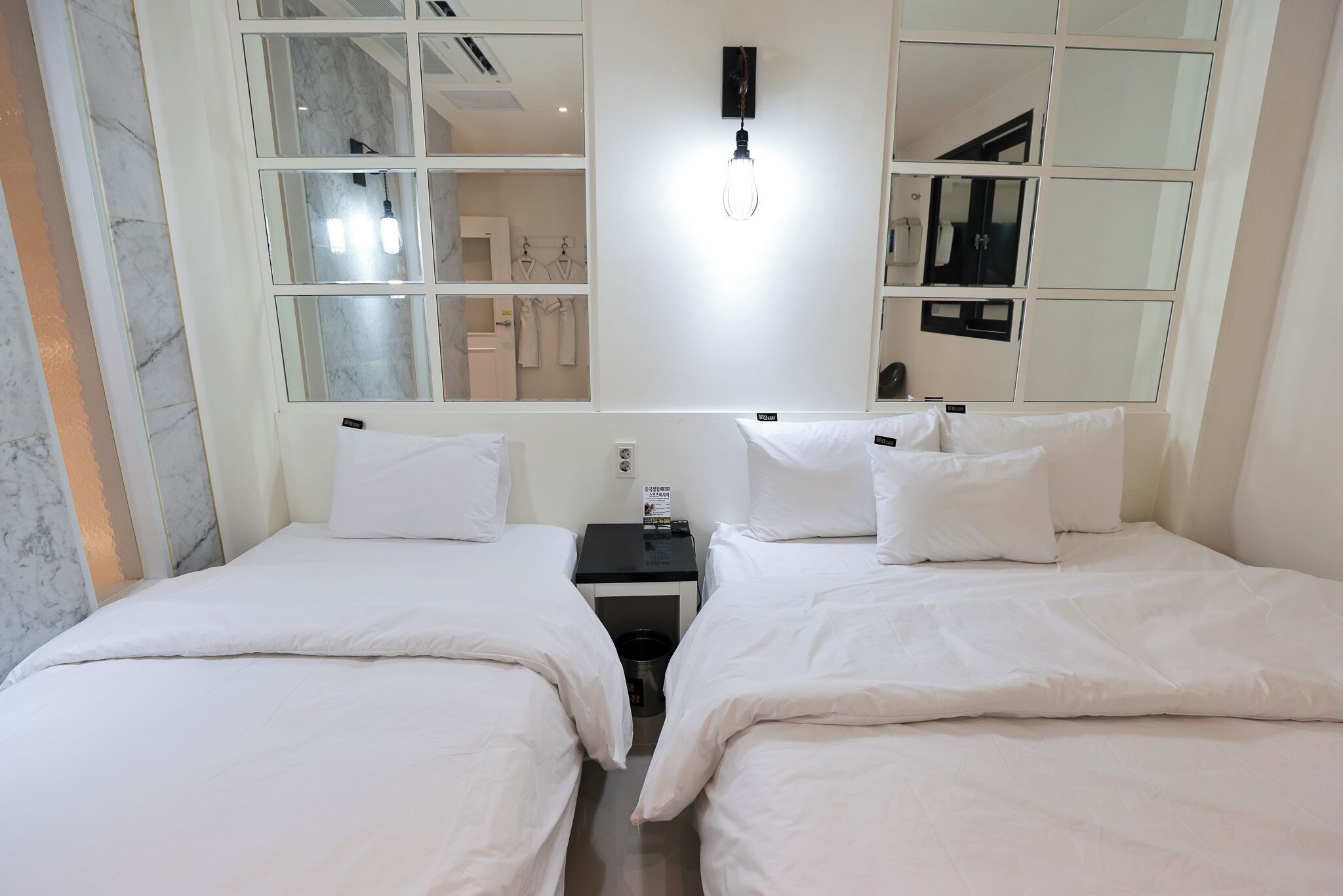 A hotel room with two beds, a nightstand, a wall-mounted light fixture, and a large mirror.