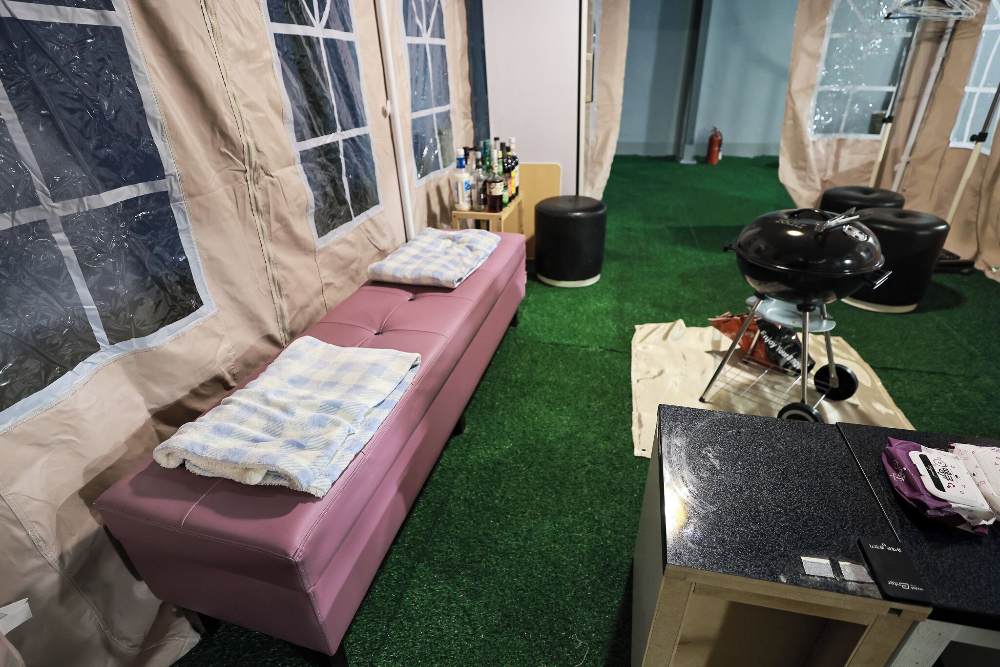 Una habitación con un sofá rosa, una mesita con cubierta negra y una estructura parecida a una tienda con ventanas.