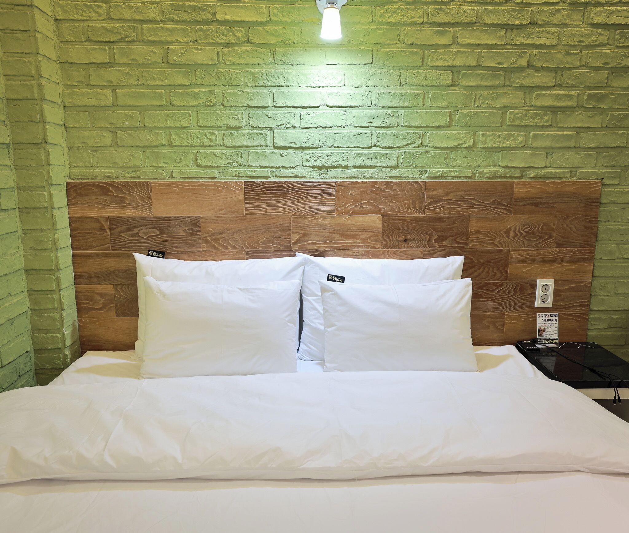Una cama con ropa de cama y almohadas blancas, un cabecero de madera y una pared de ladrillo verde.