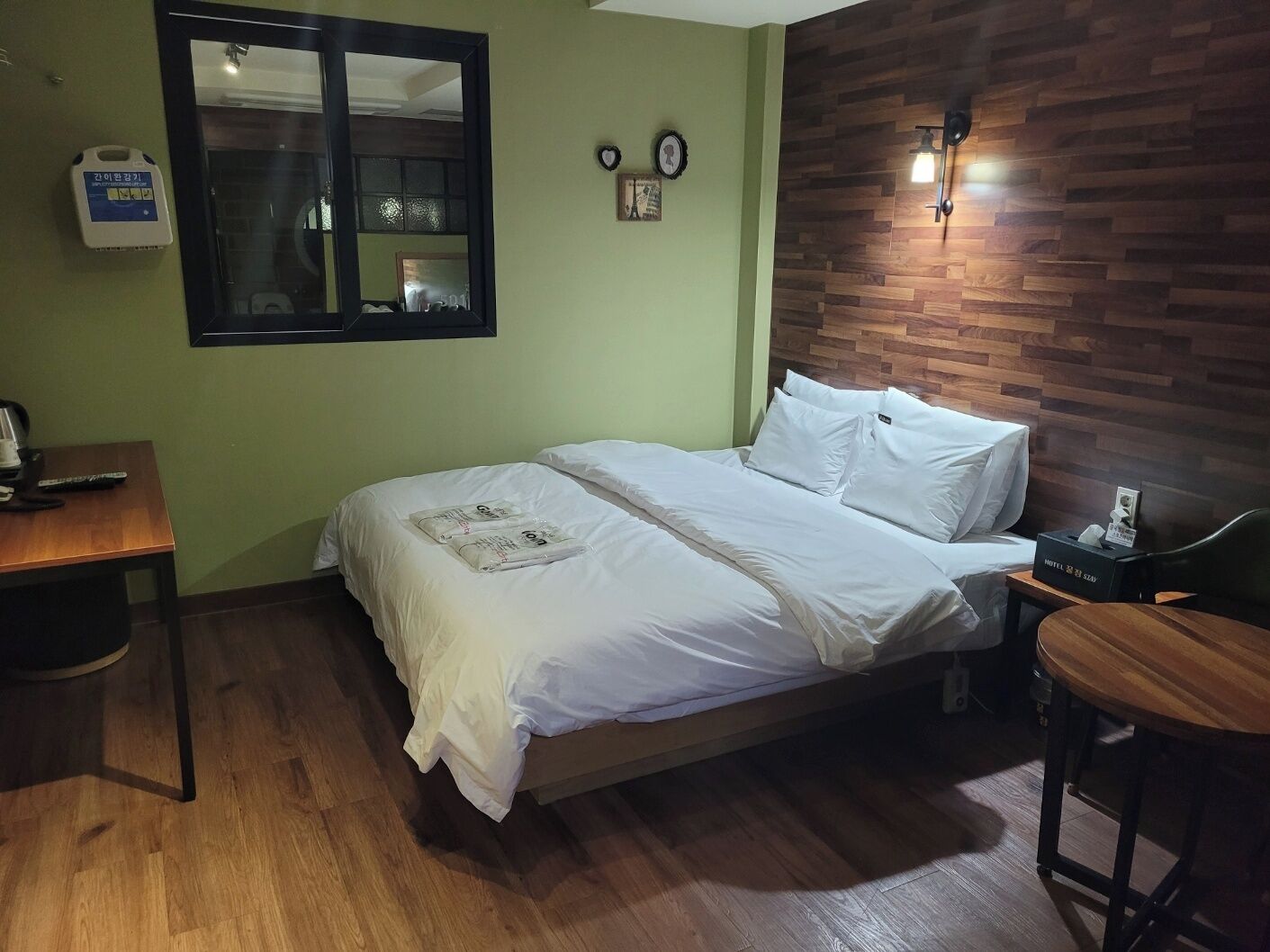 A hotel room with a bed, a desk, a chair, a mirror, and a wooden wall.