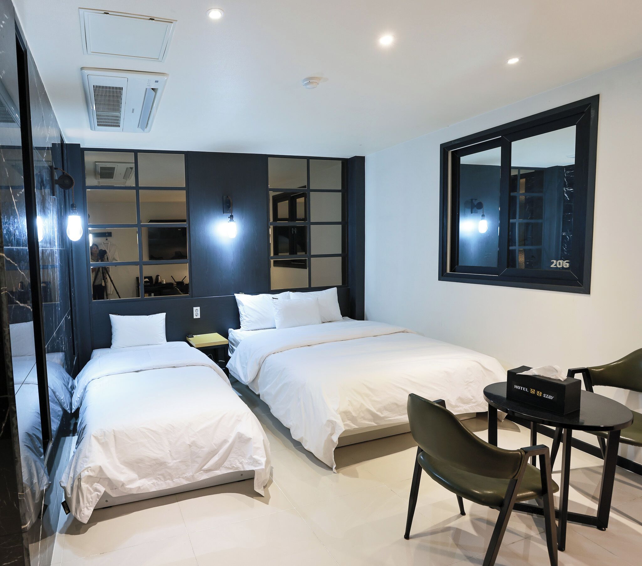 A hotel room with two beds, a desk, a chair, a mirror, and a window with the number 206.