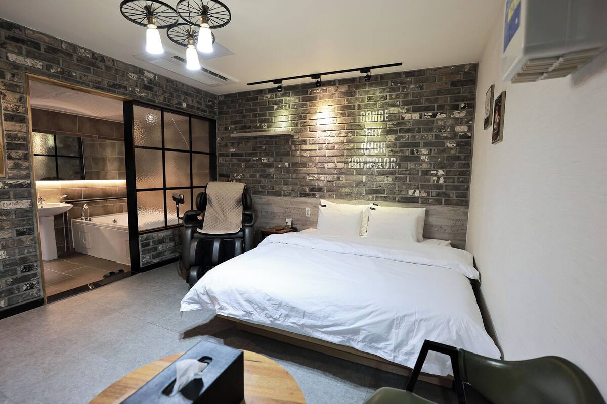 Een moderne slaapkamer met een groot bed, een inbouwbank, een kleine tafel en een zichtbare badkamer met een bad.
