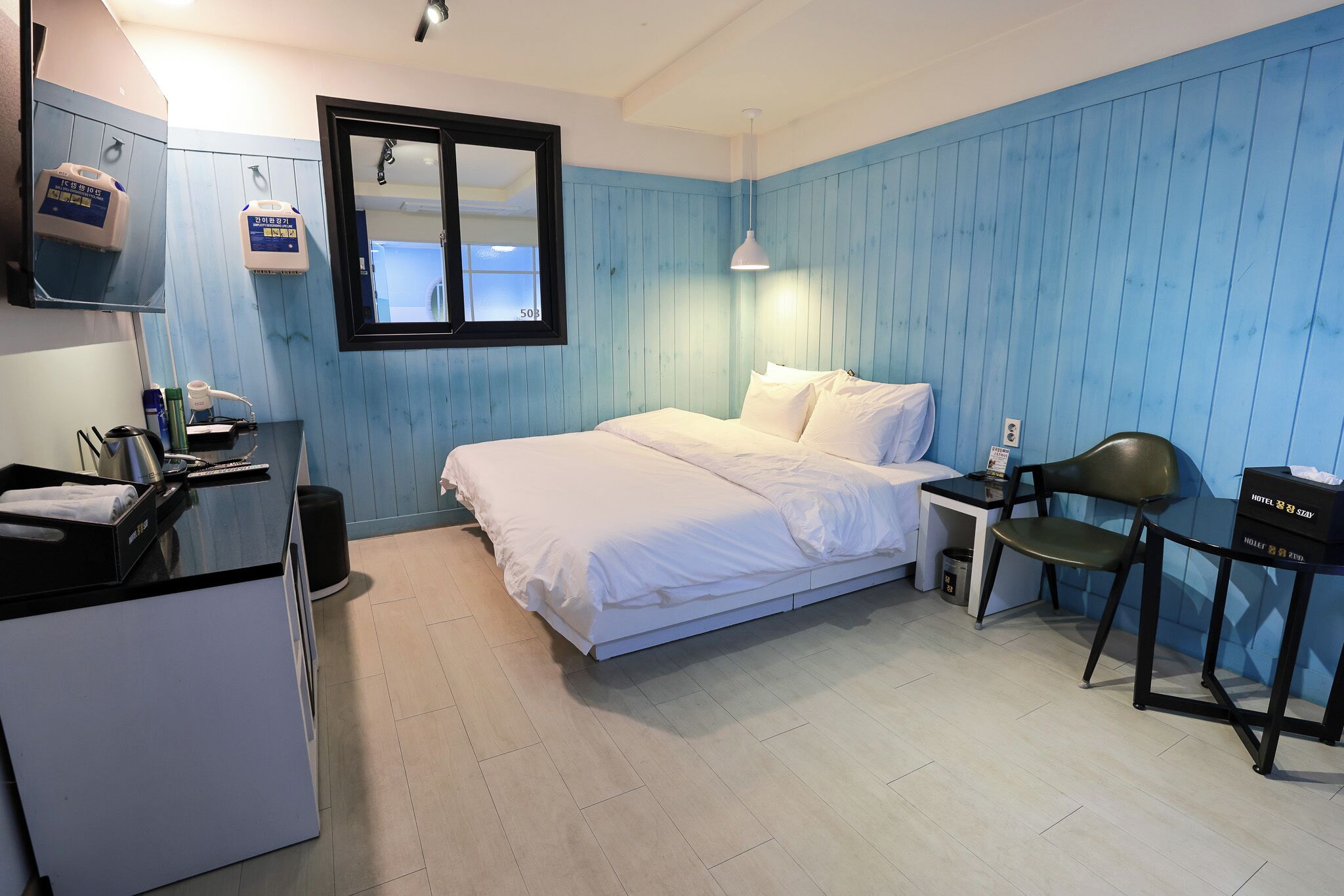 A compact hotel room with a bed, a desk, a chair, and a small kitchenette.