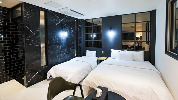 Une chambre d’hôtel moderne avec deux lits, un mur décoratif en marbre noir et une grande fenêtre donnant sur la ville.