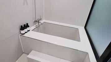 Un baño moderno con una bañera, ducha y un juego de artículos de tocador al borde.
