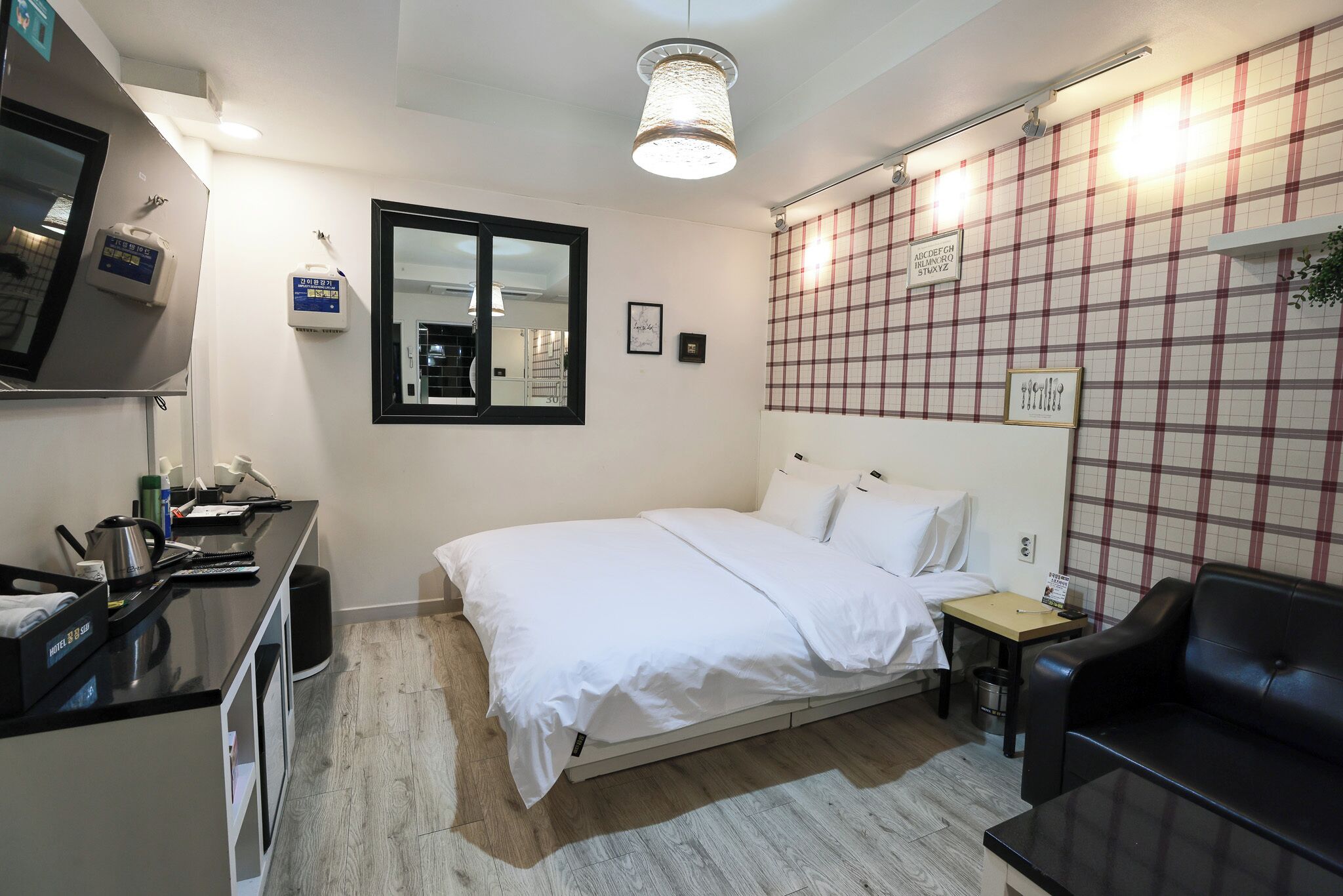 A hotel room with a bed, a desk, a chair, a small table, a trash bin, and a wall-mounted TV.