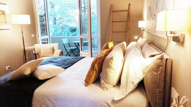 A hotel room with a bed, pillows, a chair, a radiator, and a view of trees through the window. - QuickHome - Le due Palme (Biella)