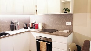 A compact kitchen with white cabinets, a built-in oven, a stovetop, and a sink. - QuickHome - Le due Palme (Biella)