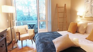 A hotel room with a bed, two chairs, a desk, a ladder, and a view of the outdoors. - QuickHome - Le due Palme (Biella)