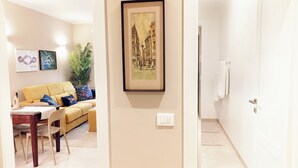 A living room with a yellow sofa, a dining table with chairs, a framed artwork on the wall, and a potted plant. - QuickHome - Le due Palme (Biella)