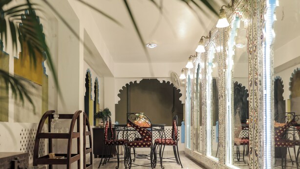 A dining area with a table and chairs, a decorative mirror, and a ceiling fan. - Roop Mahal Homestay (Udaipur)