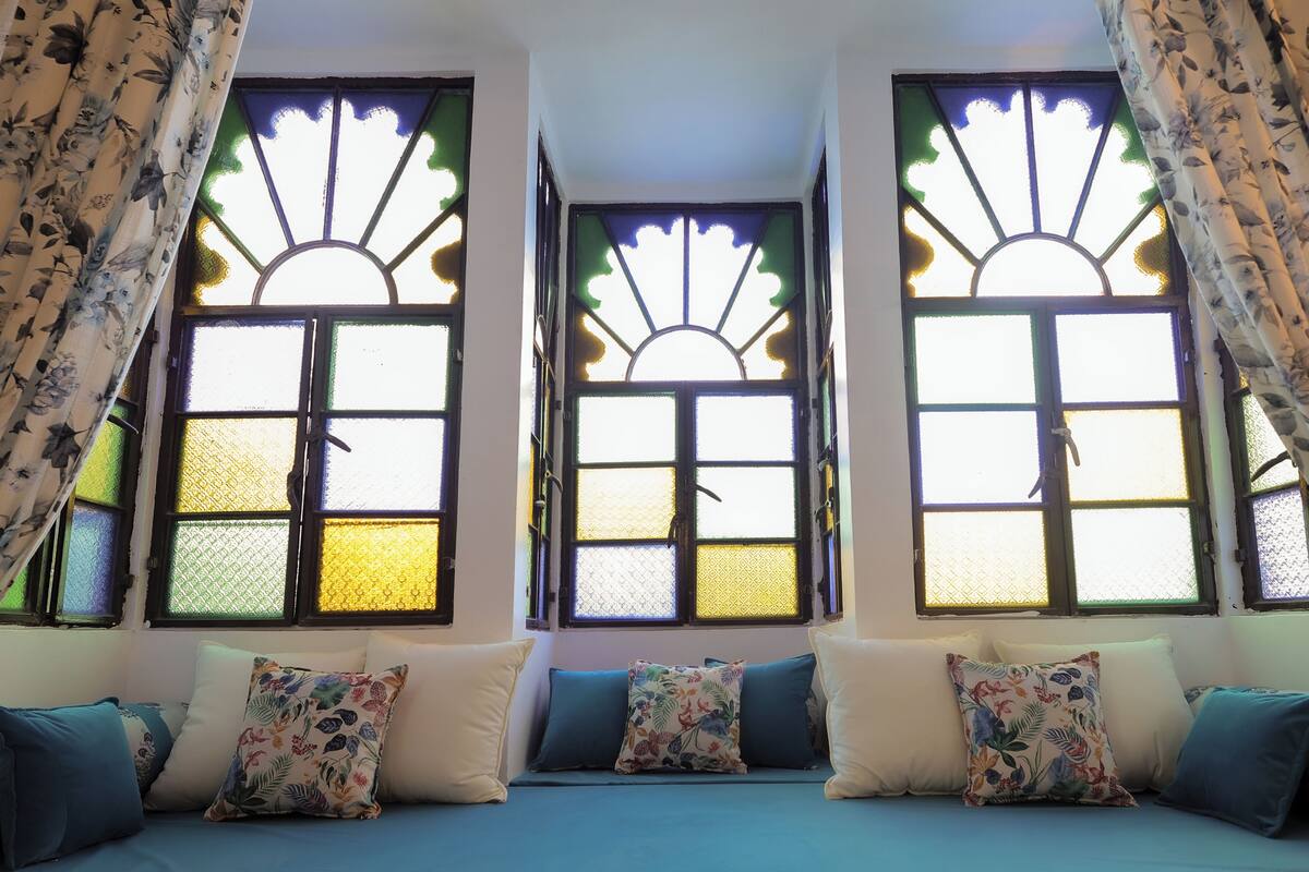 A room with a bed, floral-patterned pillows, and three windows with decorative glass panes.
