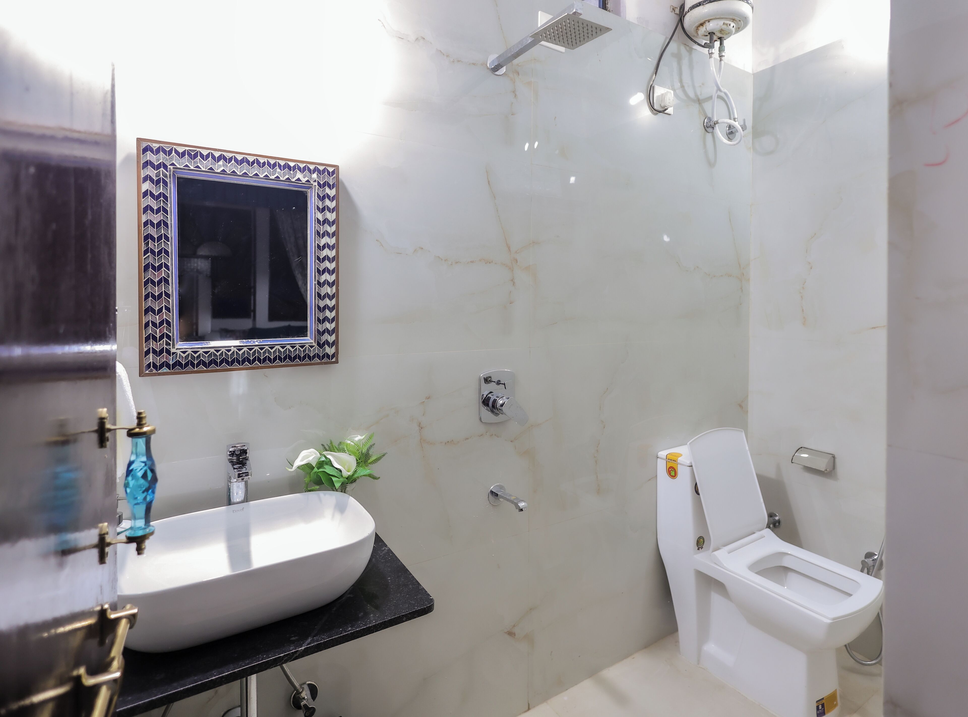 Et badeværelse med en hvid vask, toilet, brusebad og et spejl med udsmykket ramme.