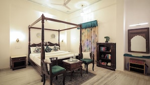 A four-poster bed with a nightstand, a small table, two chairs, a bookshelf, and a decorative mirror. - Roop Mahal Homestay (Udaipur)
