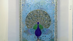 A wall with a mosaic artwork of a peacock, two potted plants, and a small decorative bowl. - Roop Mahal Homestay (Udaipur)
