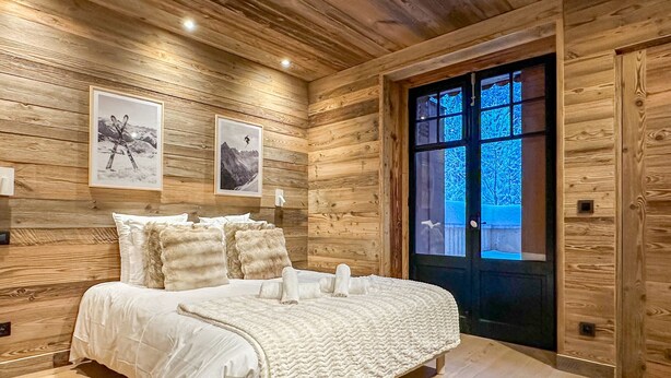 Een slaapkamer met houten lambrisering, een bed, twee ingelijste foto's en een deur met uitzicht.
