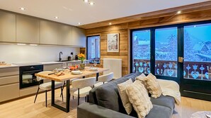 Een moderne keuken met een eethoek, een bank en uitzicht op een besneeerd landschap door grote ramen.