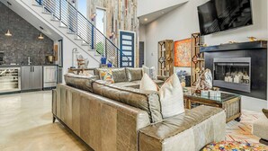 A modern living room with a leather sofa, a fireplace, a large TV, and a staircase leading to an upper level.