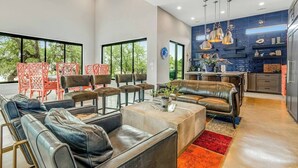 A modern living room with leather sofas and chairs, a coffee table, and a kitchen area with pendant lights and a blue backsplash.