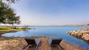 Two beach chairs facing a calm lake with a clear sky.