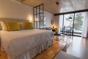 Un dormitorio moderno con una cama grande, un balcón con mesa y sillas, y vistas a la ciudad.