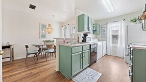 Una cocina con armarios verdes, una zona de comedor con mesa y sillas, y una pequeña isla con un fregadero.