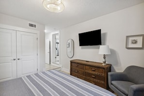 Une chambre à coucher avec un lit, une commode, un téléviseur et une chaise.