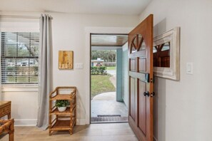Ein Durchgang zu einem überdachten Außenbereich mit einer Holztür, einem Fenster mit Rollläden und einem Korbschrank mit einer Pflanze.