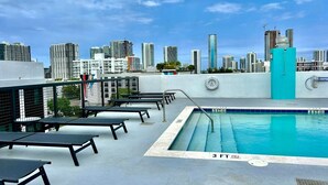 Piscina en la azotea con vista al horizonte de la ciudad, sillas de descanso y un flotador.