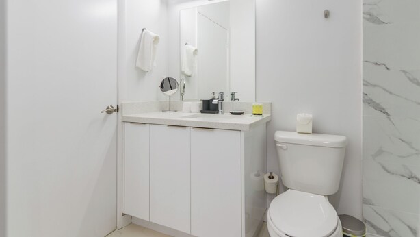 Un baño moderno con lavamanos, espejo y retrete blancos.