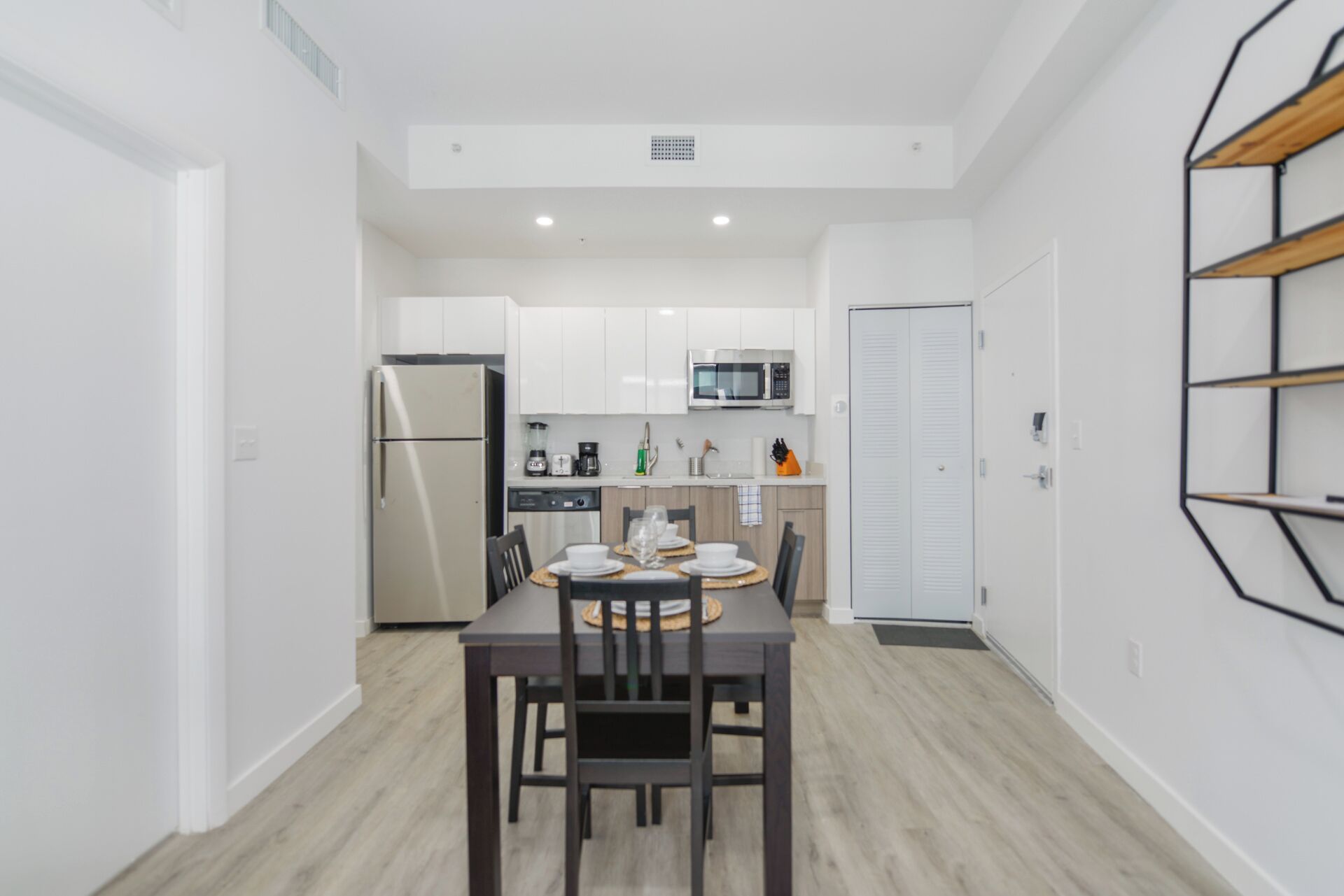 Una cocina moderna con armarios blancos, un refrigerador, un microondas y un comedor con una mesa preparada para cuatro.