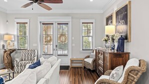 A room with a ceiling fan, three windows with blinds, a sofa, a chair, a wooden cabinet, and a lamp. - Seagrove Gardens Mins to the Beach, Santa Rosa Retreat w/ A+ Design (Santa Rosa Beach)